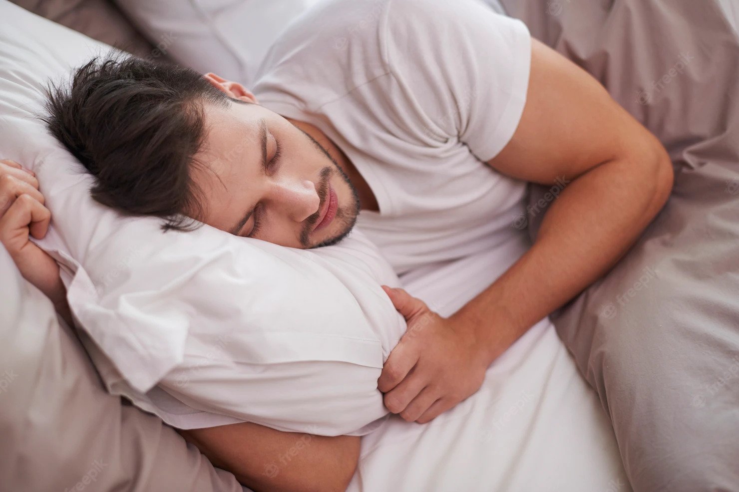 man sleeping with pillow and tan comforter